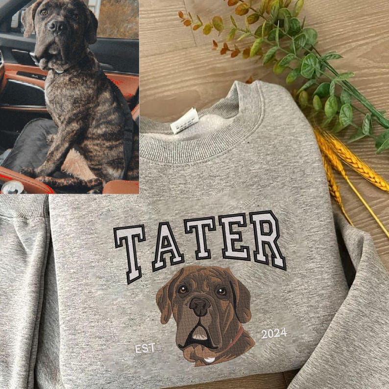 Felpa grigia personalizzata con ricamo a colori del ritratto di un cane, realizzato a partire dalla foto del cane mostrata nell’angolo superiore sinistro; design con il nome “Tater” e l’anno “2024”.