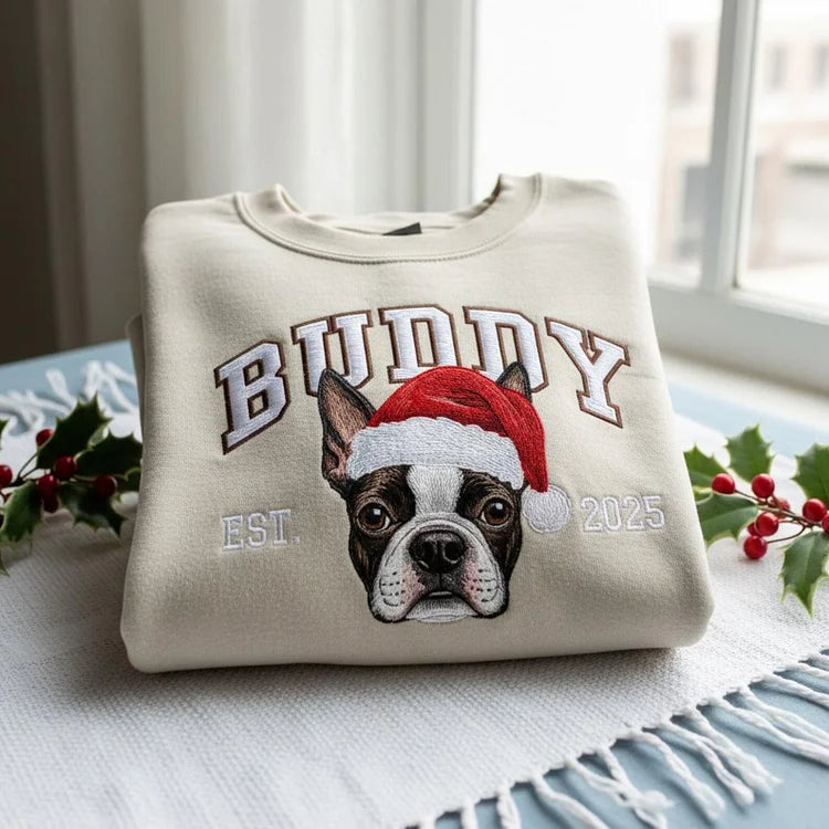 Felpa personalizzata color crema con ritratto del cane ricamato a colori e cappello di Natale, nome “BUDDY” e dettaglio “EST. 2025”.
