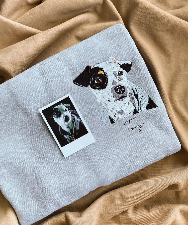 Una felpa grigia personalizzata con cappuccio presenta un ritratto di un cane ricamato a colori e il suo nome sul lato sinistro del petto, a dimostrazione di come una fotografia possa essere trasformata in un ricamo raffinato | Doniunici