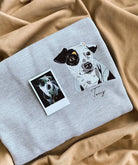 Una felpa grigia personalizzata con cappuccio presenta un ritratto di un cane ricamato a colori e il suo nome sul lato sinistro del petto, a dimostrazione di come una fotografia possa essere trasformata in un ricamo raffinato | Doniunici